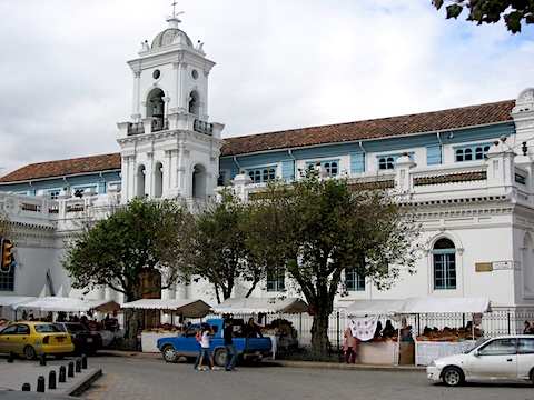 A bell tower is in the middle of the front of the         building and vendors line the street.