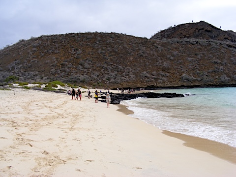 The beach is a broad stretch of sand with             a hill of volcanic rock behind it