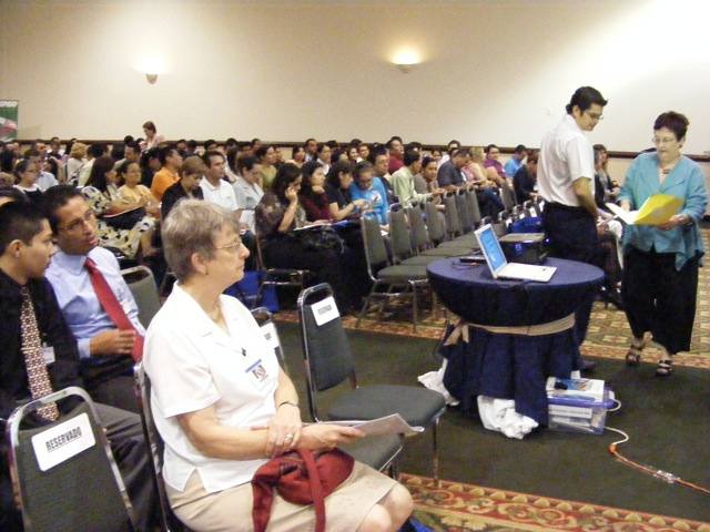 People gathering for the opening ceremony of the                   conference. Gail is sitting in a reserved seat in                  the front row, and the first speaker                  is getting set up.