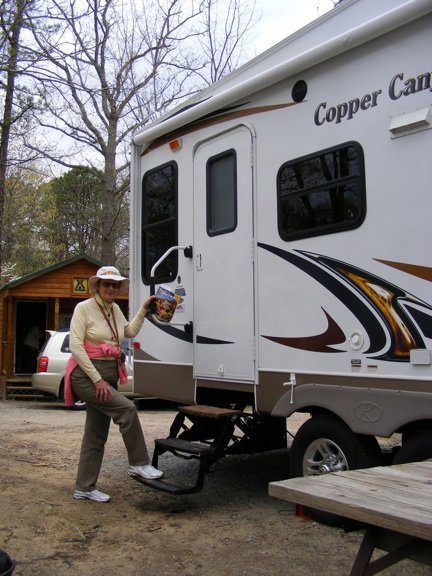 Gail is mounting the             steps to our door. The awning remains rolled up            at the top of the trailer's side wall.