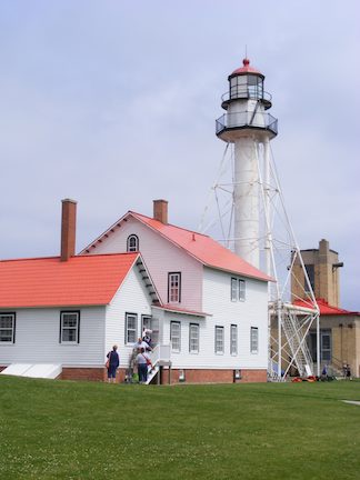 The light sits atop a white column,
               with four legs bracing it. There are
               circular walkways around the light and
               one level down. In the photo, a white
               two-story building with a red roof is
               to th left of the light.