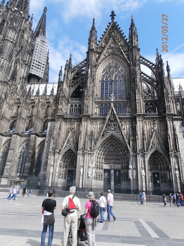 Across a nearly empty plaza, the ornate exterior of the cathedral            rises toward a blue sky. The base of the bell towers can be seen            on the left of the photo.