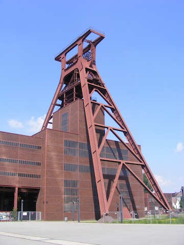 A barn red A-frame tower straddles a rusty red building in front of              a deep blue sky