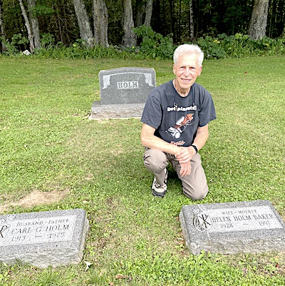 Al kneels on one knee behind his motherss stone. His dadss stone is            to theh left and the Holm monument behind him