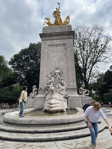 This is a tall stone monument with a fontain at the bottom and gilded                 figures at the top