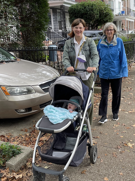 CJ is pushing Morgans stroller on a sidewalk with Morgan               in the stroller and Gail is walking beside