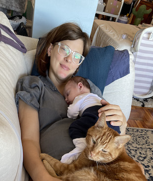 CJ is on the coach with sleeping Morgan on her chest and                 Oliver, the cat, on her lap