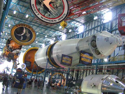 The front end of t a Saturn V rocket. The Apollo command monduleand the service module are prominent while the second and first stages disappear in the glare from the other end of the building