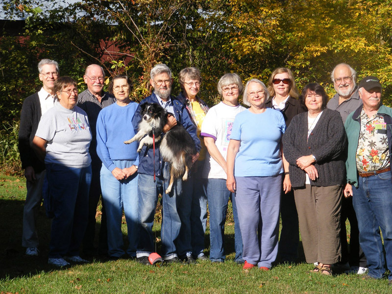The whole group in the backyard of the Guesthouse with the covered bridge in the trees behind them
